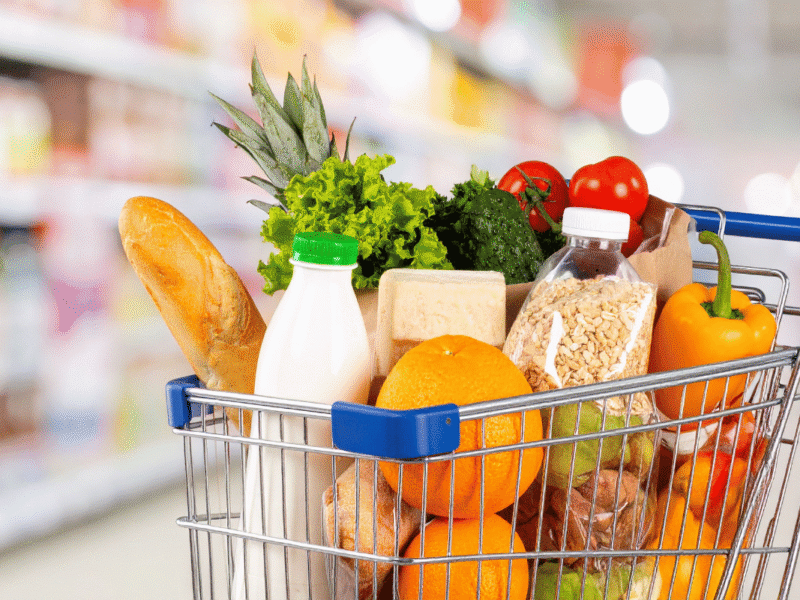 Woman grocery shopping on a budget with fresh fruits, vegetables, and healthy foods in her cart.