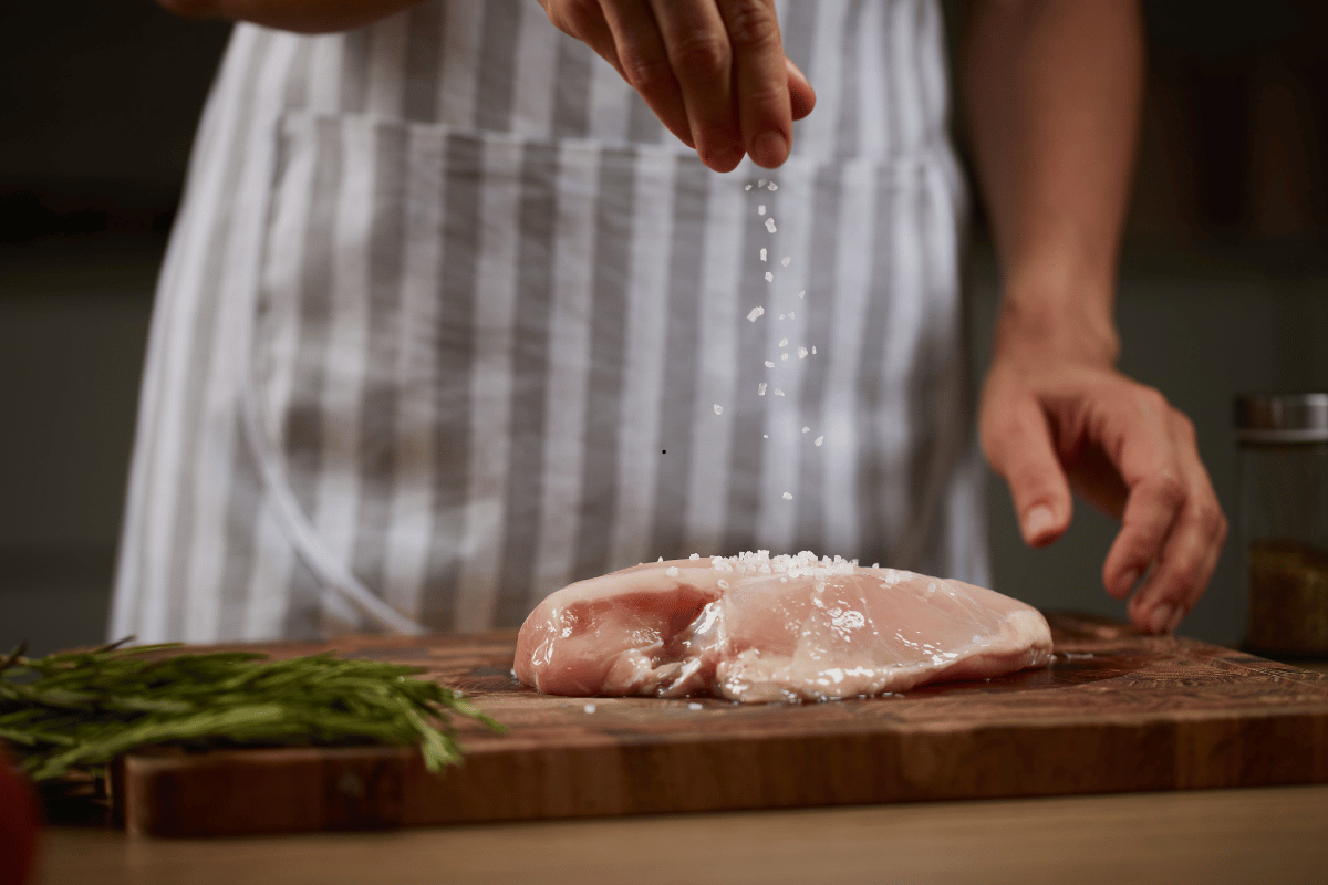 chicken breast being seasoned with spices